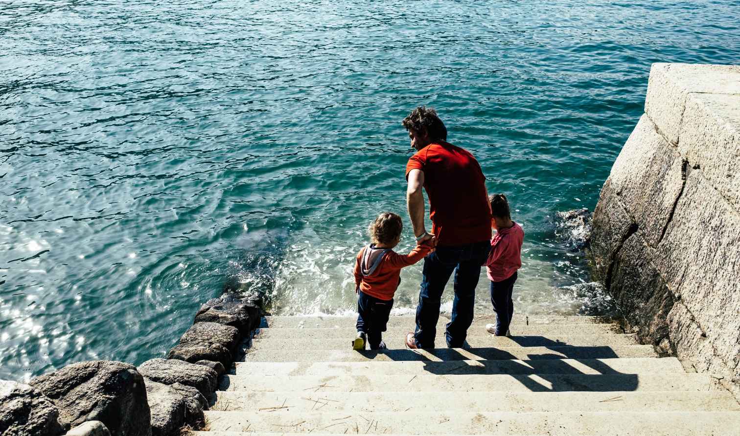 Man and two children on steps leading to a large body of water in Hiroshima