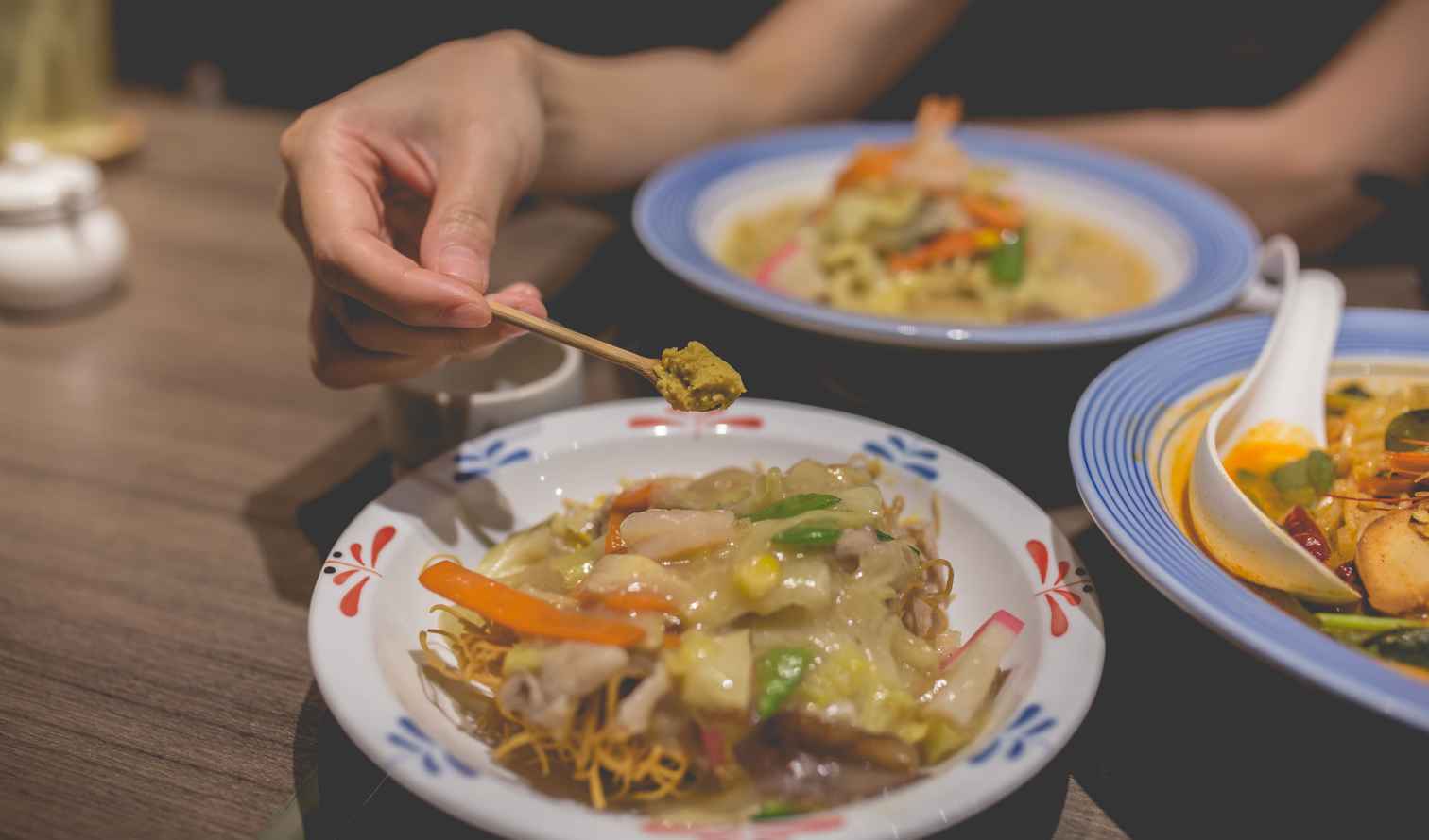 Hand holding food sample on chopstick above noodle dish in Nagasaki 