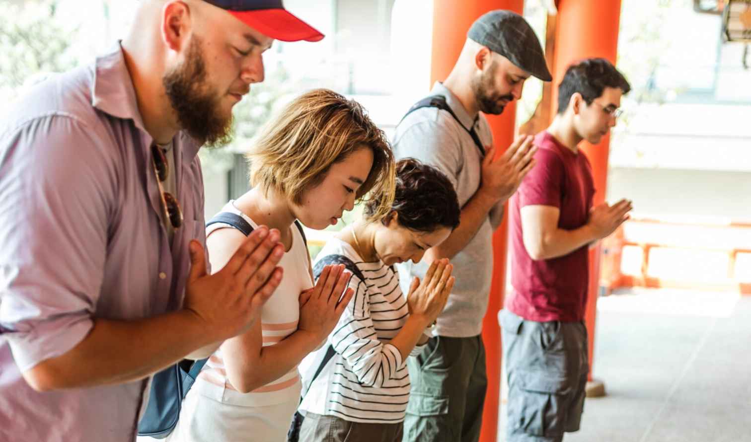 People praying at a shrine with orange columns in the background in Nagasaki