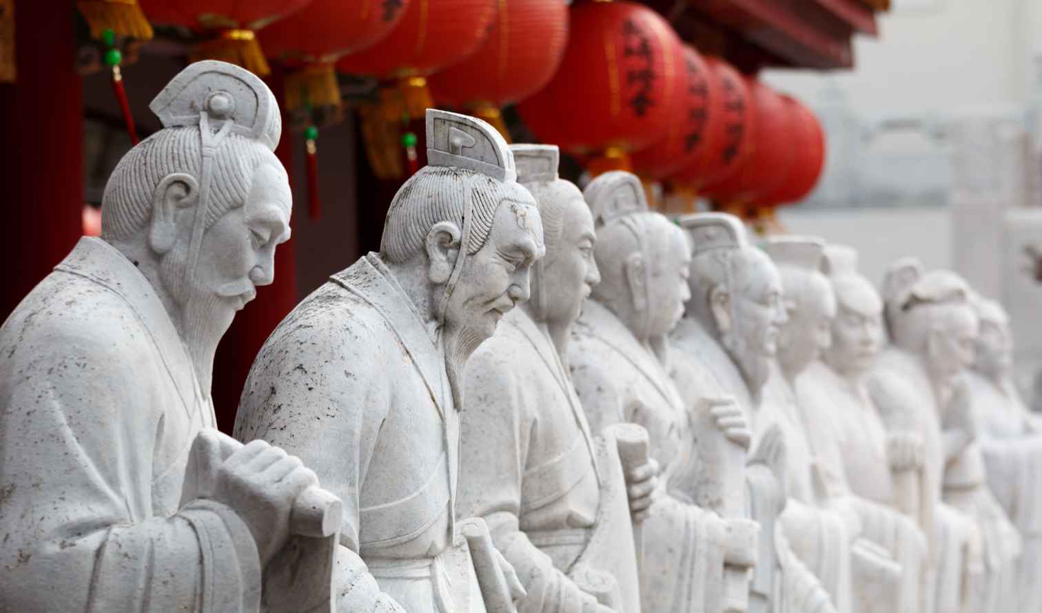 Row of stone statues depicting historical figures with red lanterns overhead in Nagasaki