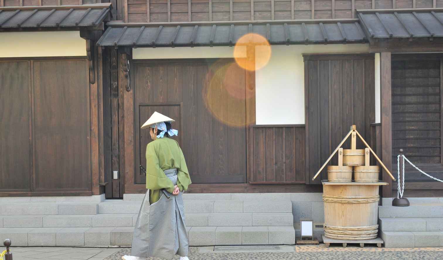 Person in traditional Japanese attire walking past wooden building facade in Nagasaki.