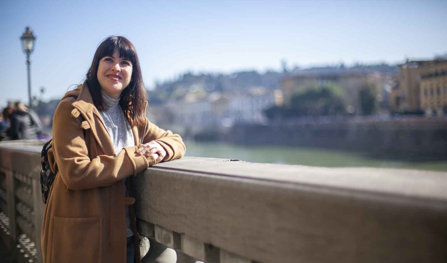 A person stands by the Arno River with Florence in the background.