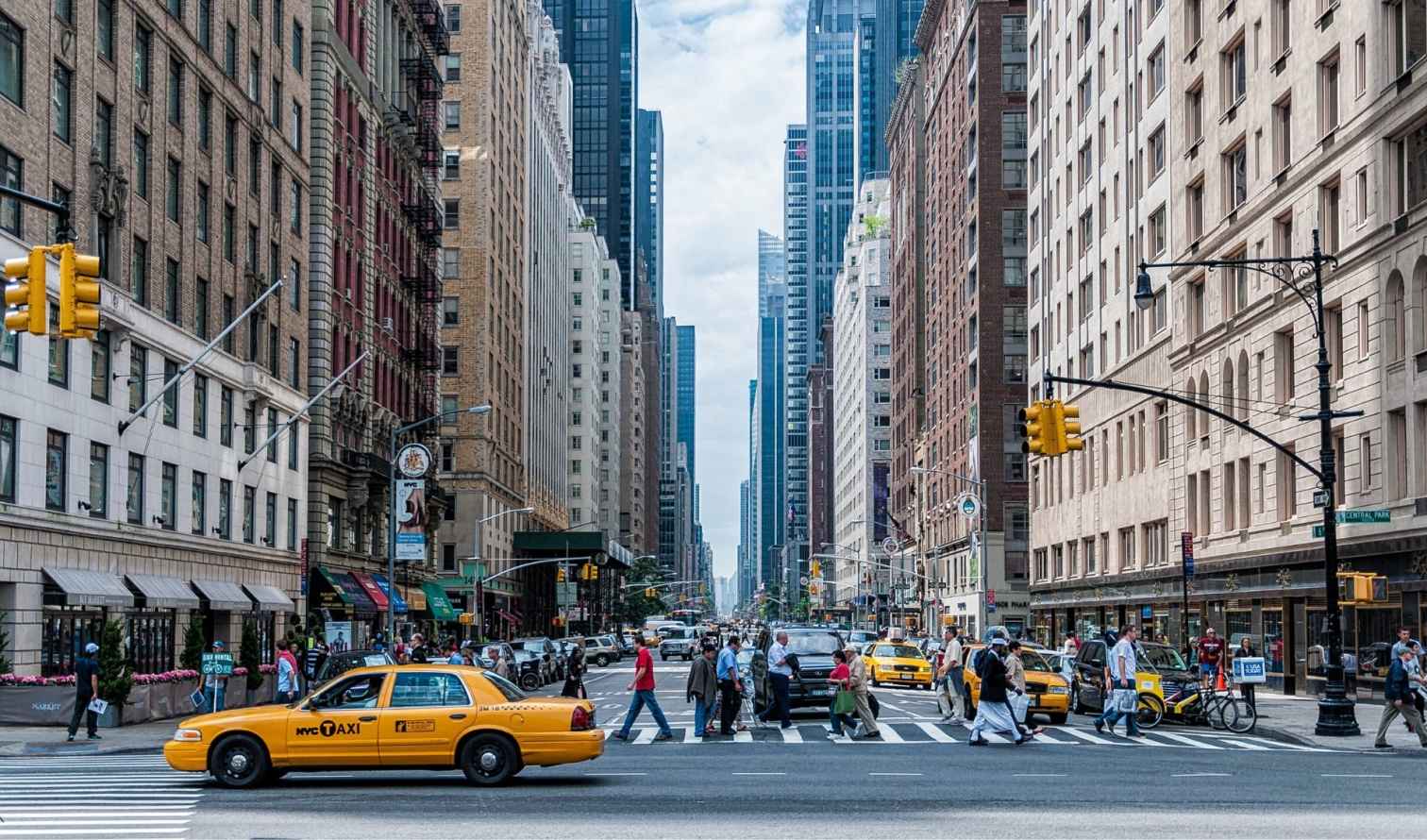 Pedestrians crossing a street in Manhattan with skyscrapers lining both sides.
