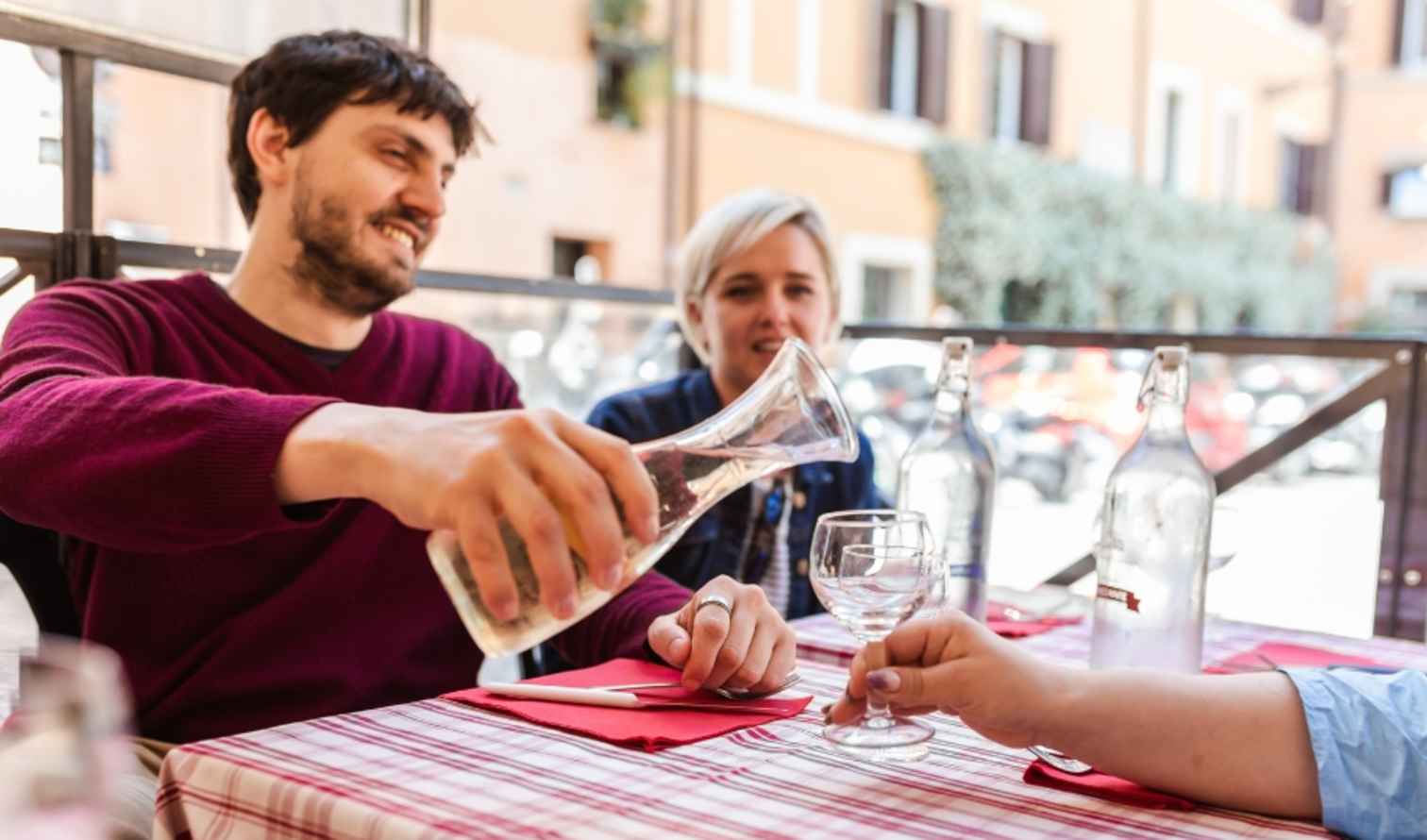 A person pours water from a carafe at an outdoor cafe in Rome.