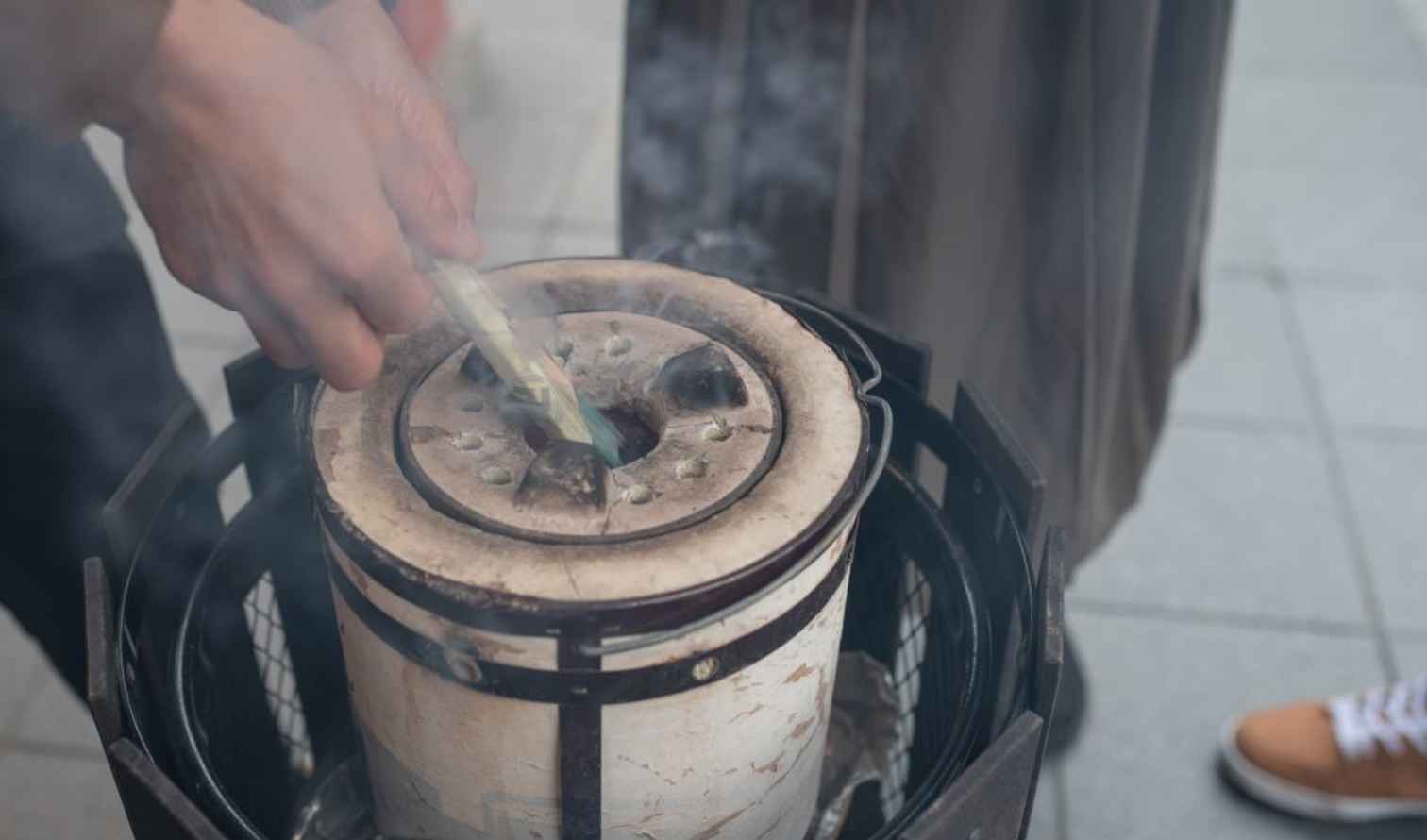 Person cooking over a small charcoal stove on a city sidewalk in Tokyo