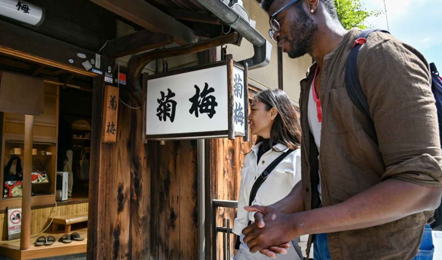 Two people walk past a wooden storefront with Japanese signs in Kyoto