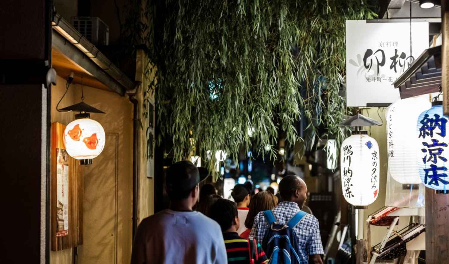 People walking through Pontocho Alley in Kyoto at night under lanterns.