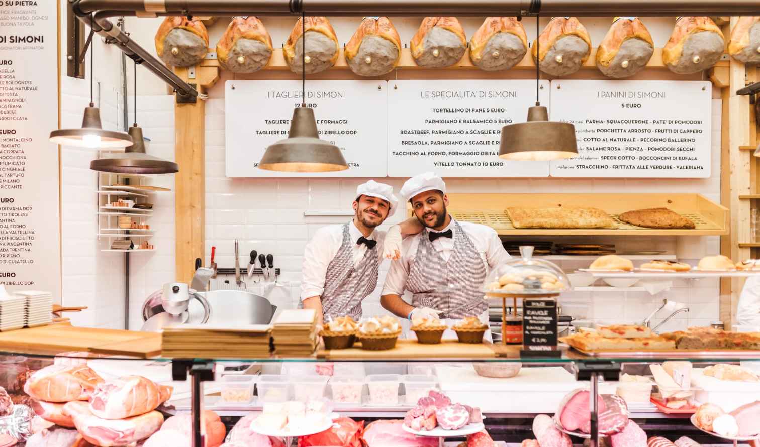 Two chefs behind a charcuterie counter at Salumeria Simoni, Bologna.