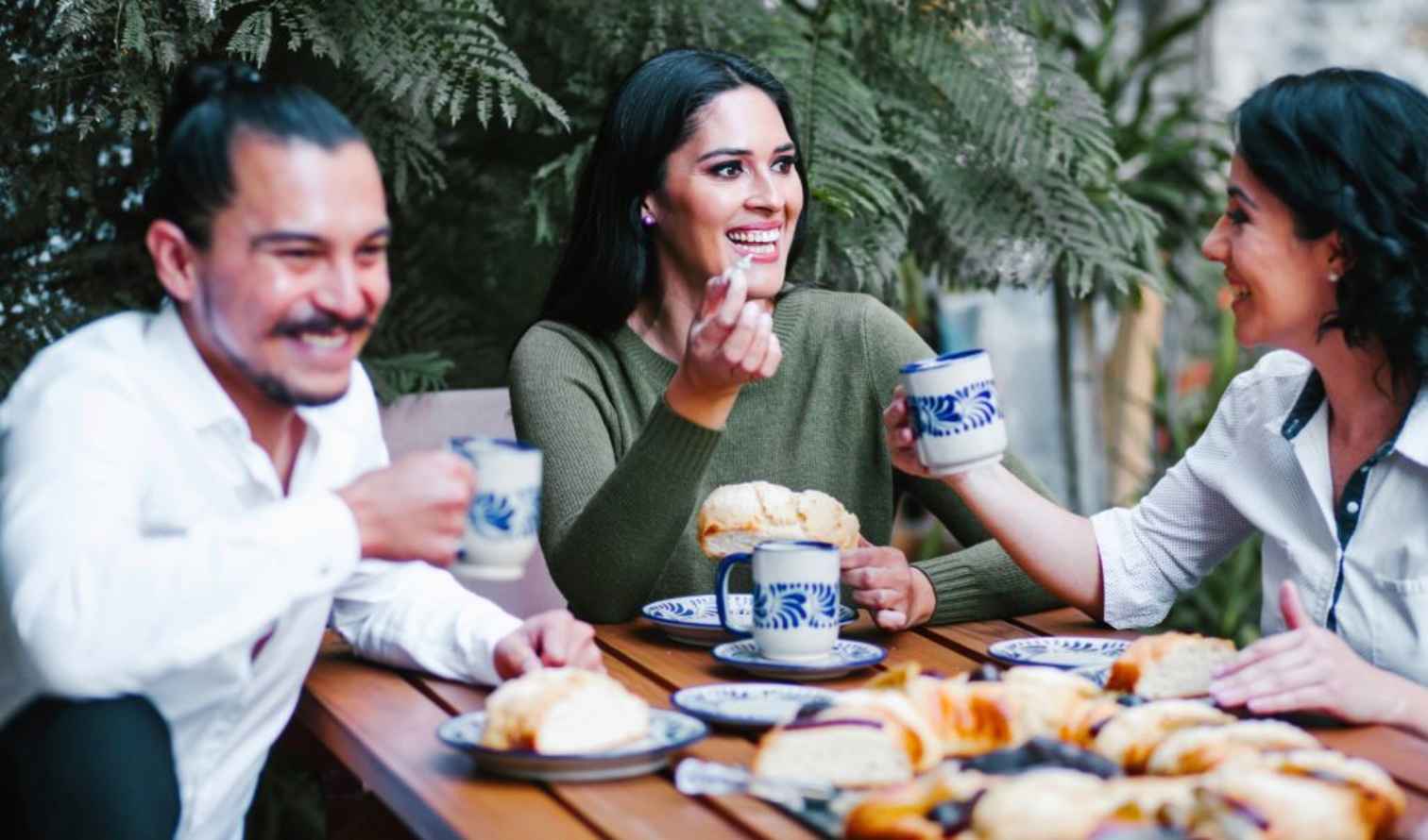 Three people sitting at a wooden table enjoying pastries and drinks in Mexico