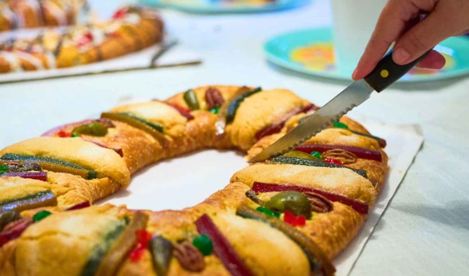 A hand slicing a Rosca de Reyes cake on a table in Mexico