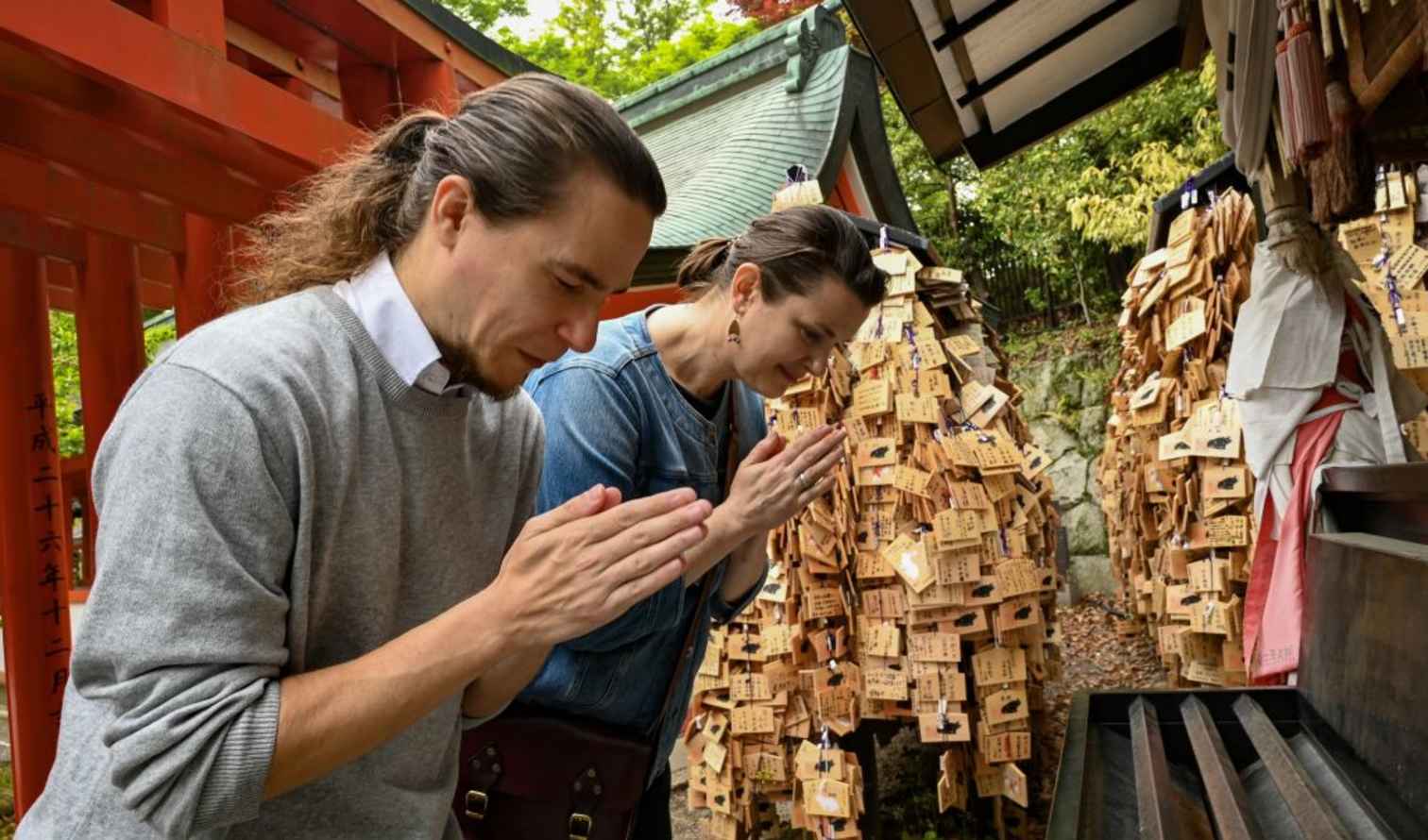 Two people praying at a Japanese shrine with ema plaques in Kyoto.
