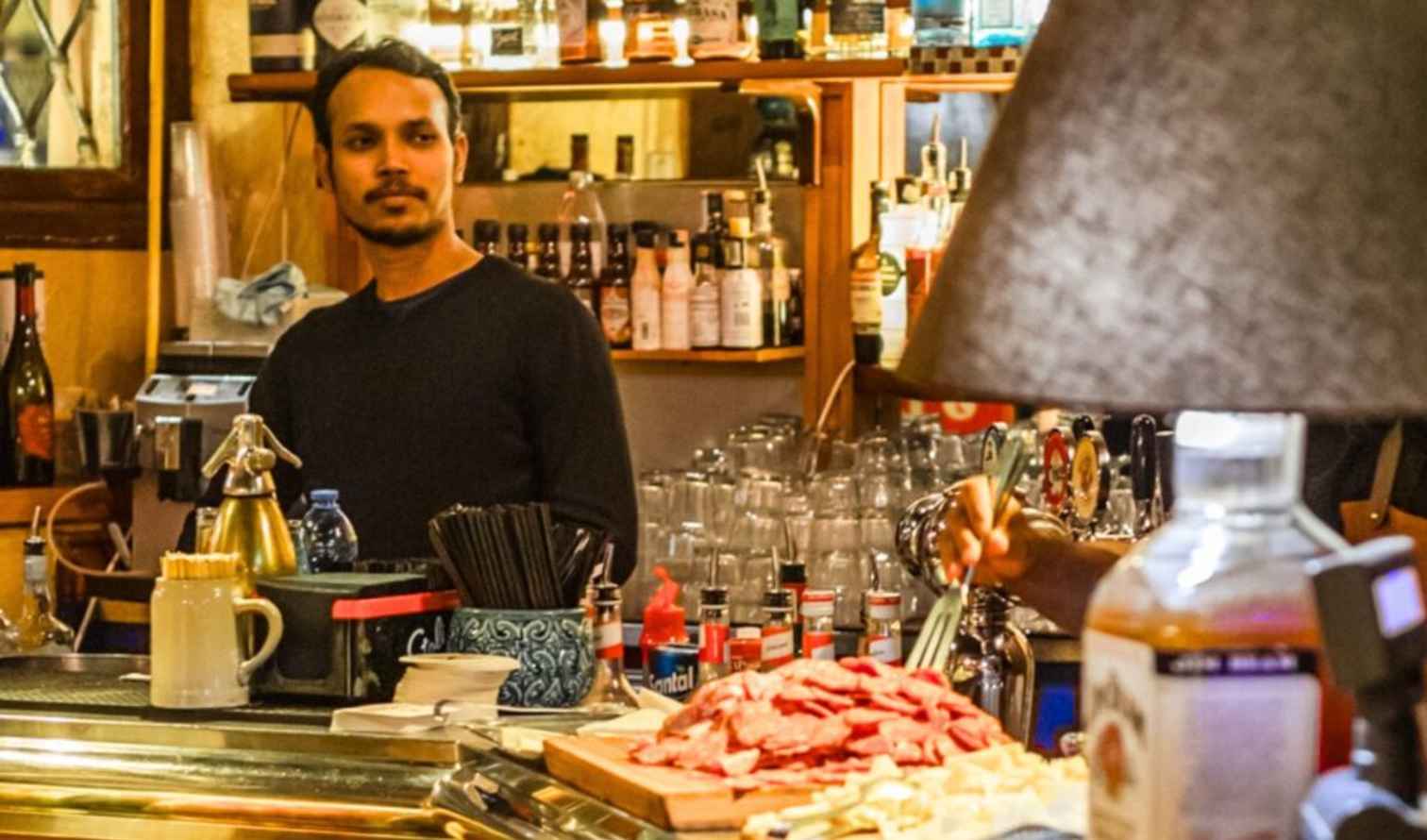 Two people behind a bar counter with various bottles and glasses in Milan