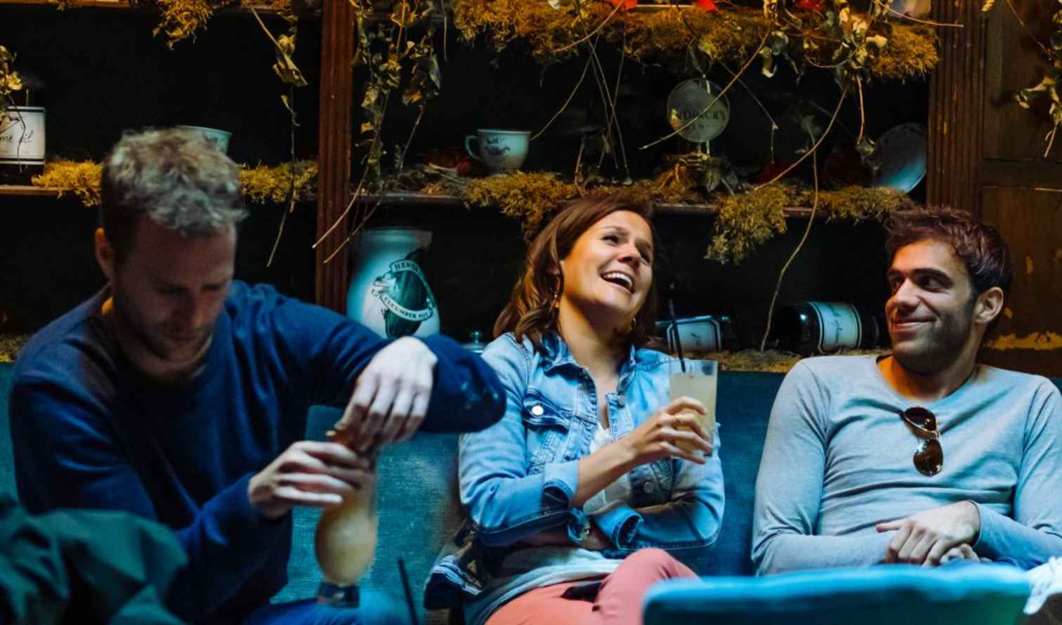 Three individuals seated casually in a room with rustic wooden shelves in Brussels