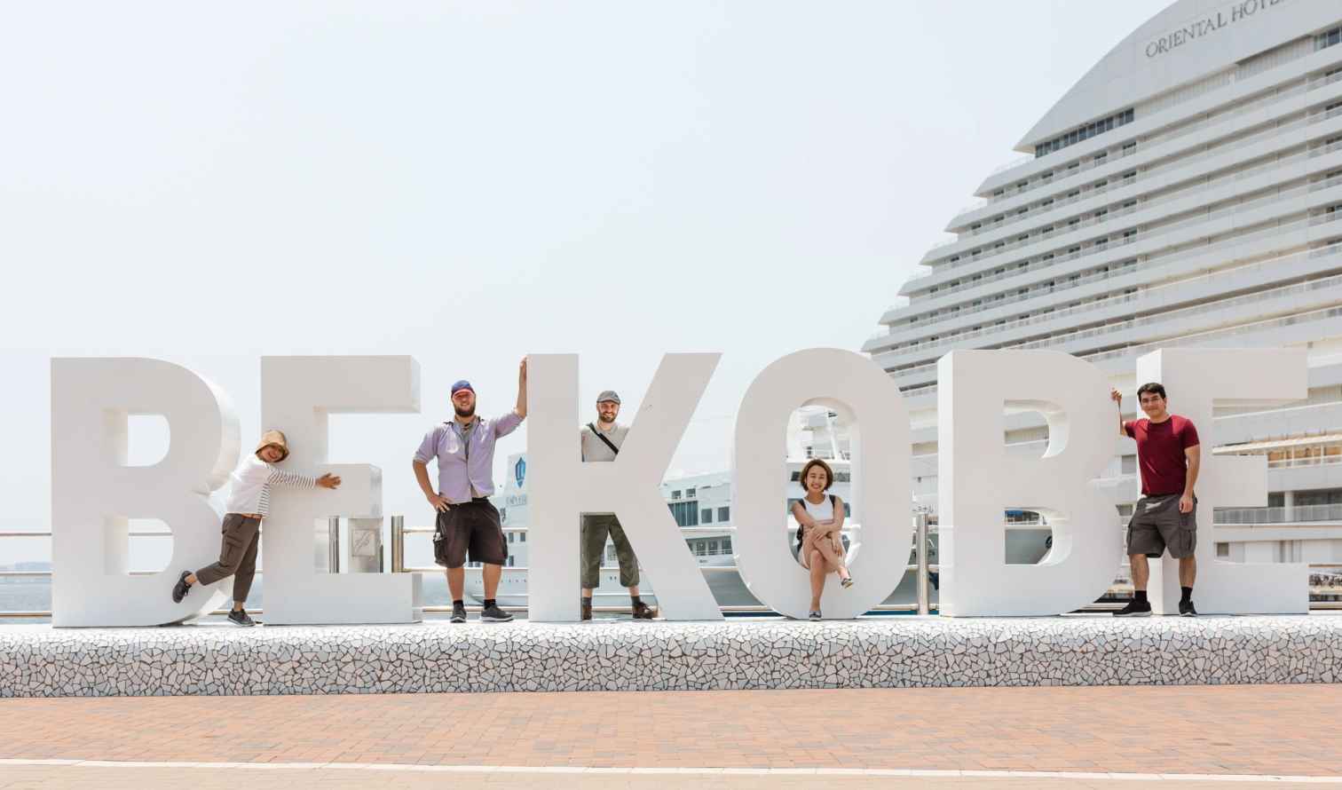 People posing on large 'BE KOBE' letters near Oriental Hotel, Kobe Harbor.