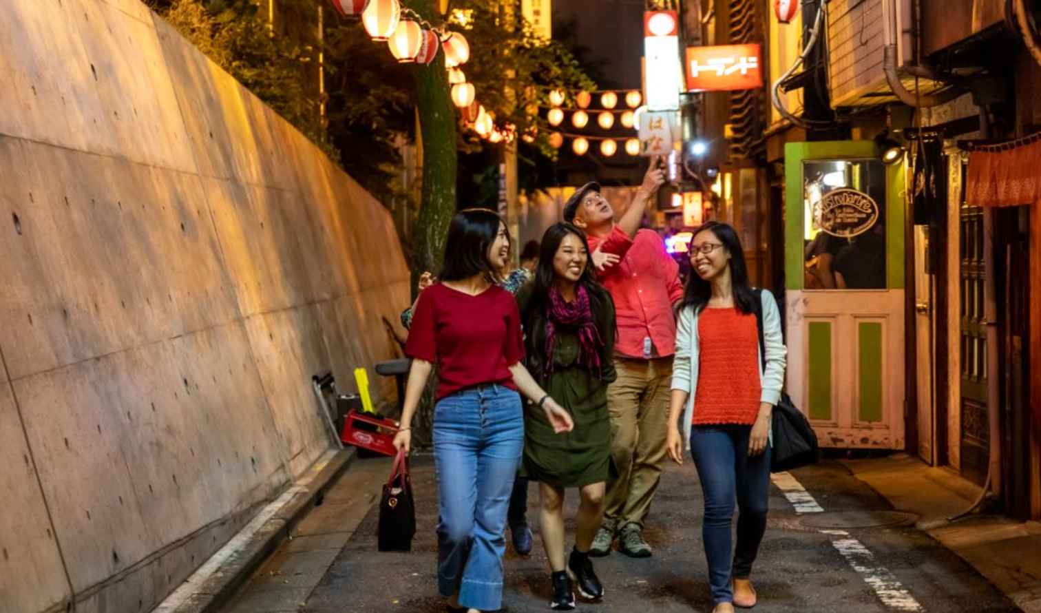 Group walking through Piss Alley, Tokyo, with paper lanterns overhead.