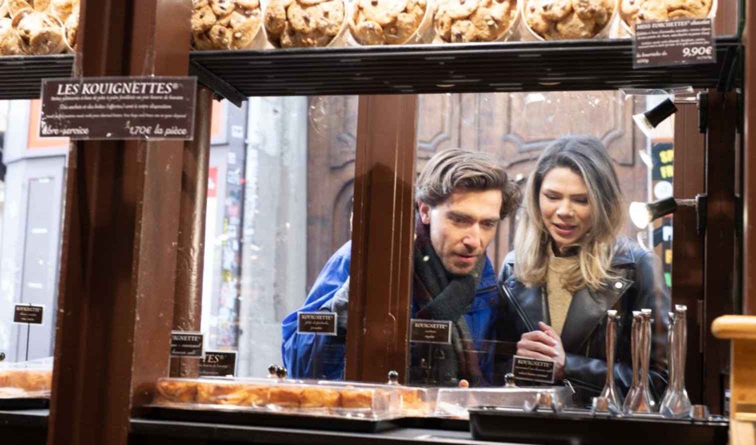 Two people looking through a bakery window in a French street in Paris