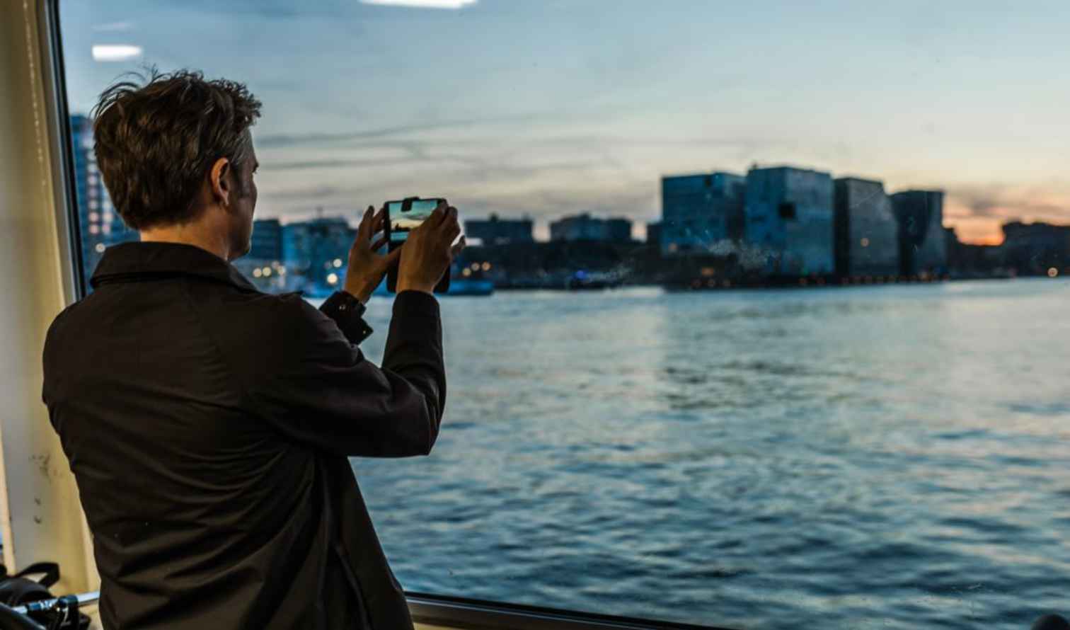 Person taking photo of waterfront buildings from a boat window in Amsterdam