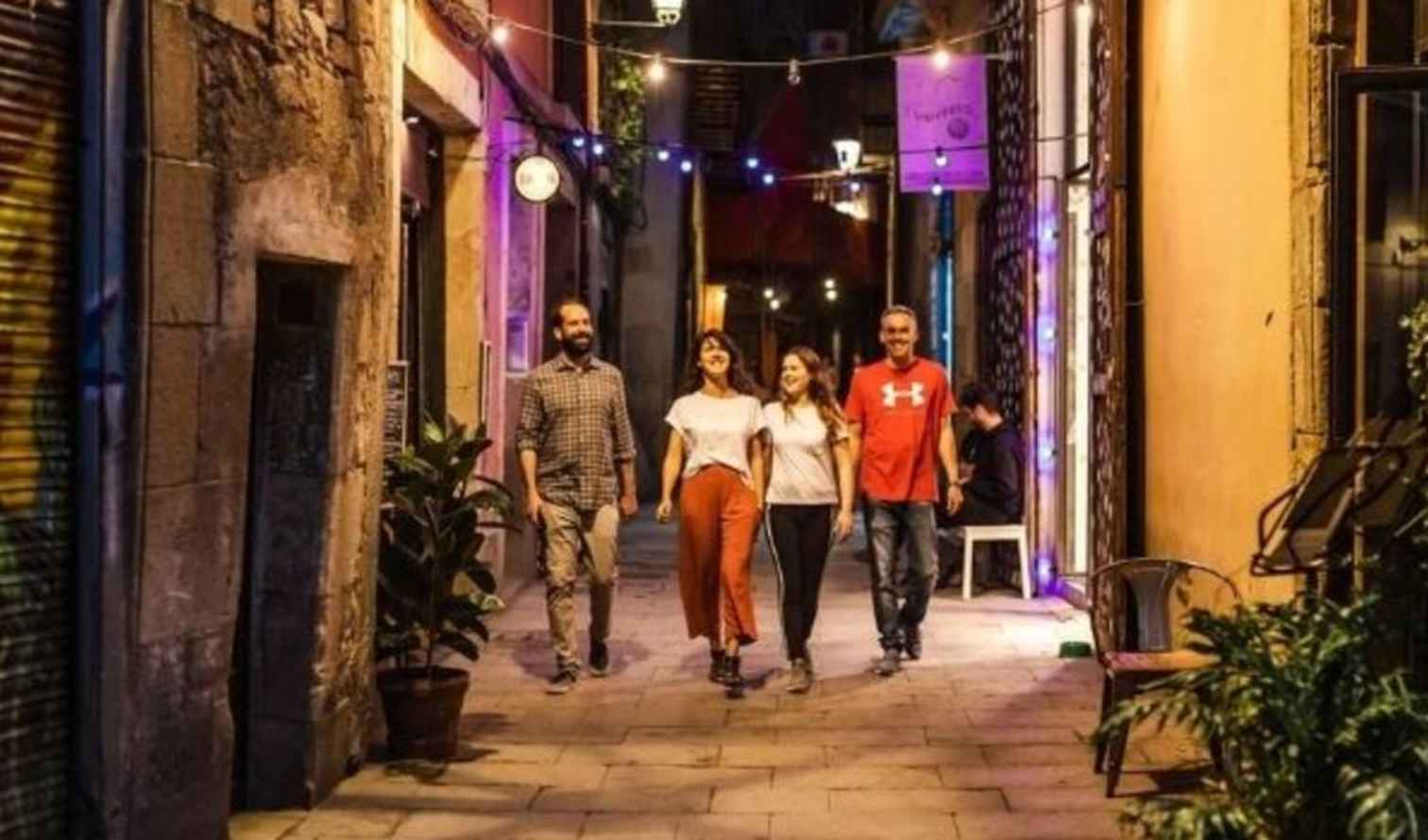 Four people walking through a narrow alleyway with string lights in Barcelona