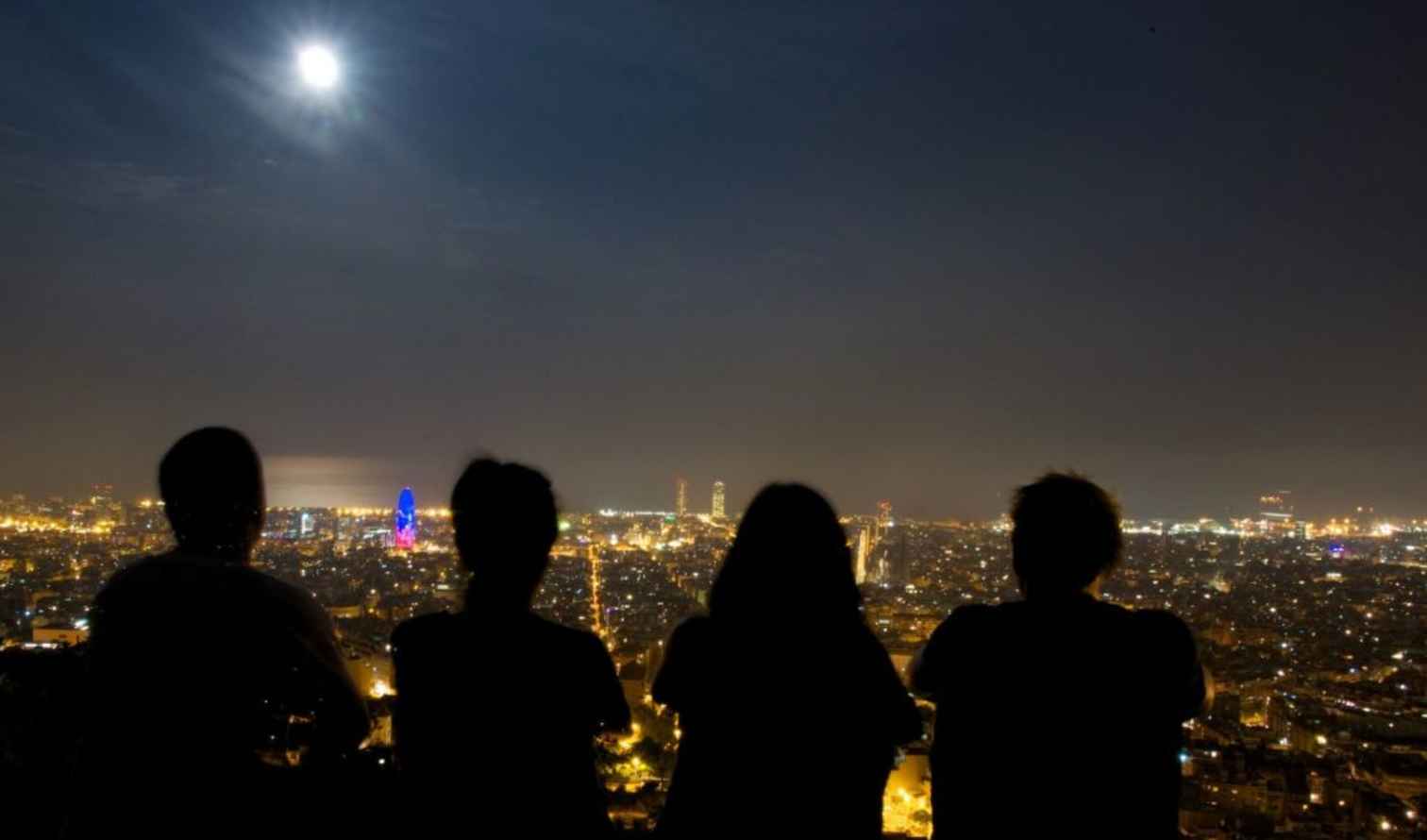 Four people silhouette against Barcelona cityscape at night.