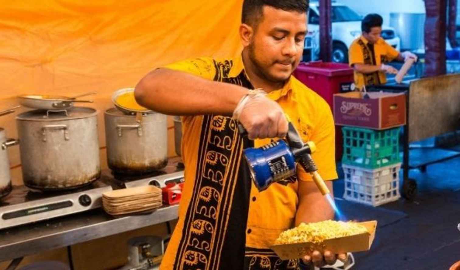 Person heating food with a blowtorch at a market setting in Melbourne