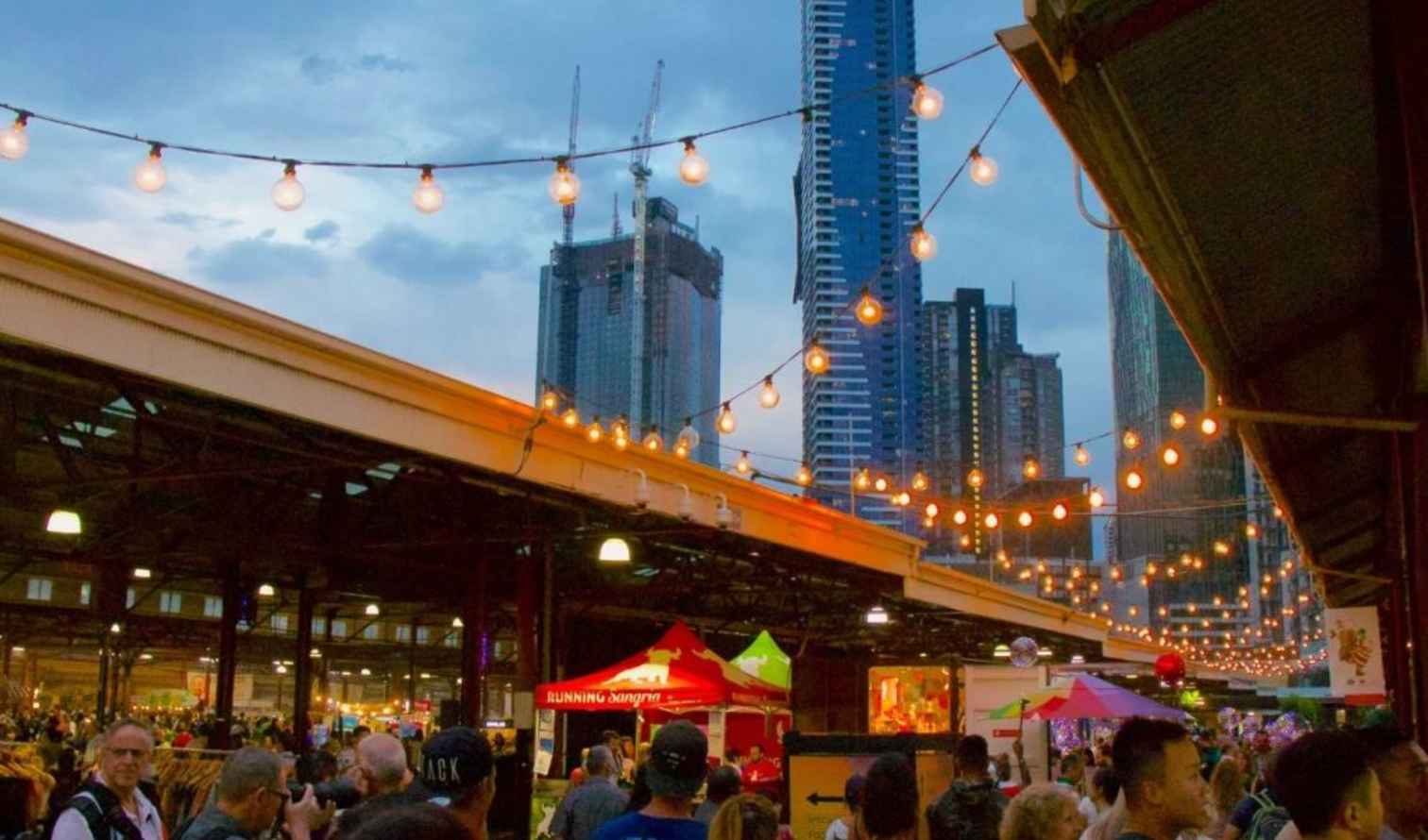 Crowded market stalls under string lights at dusk in Melbourne.