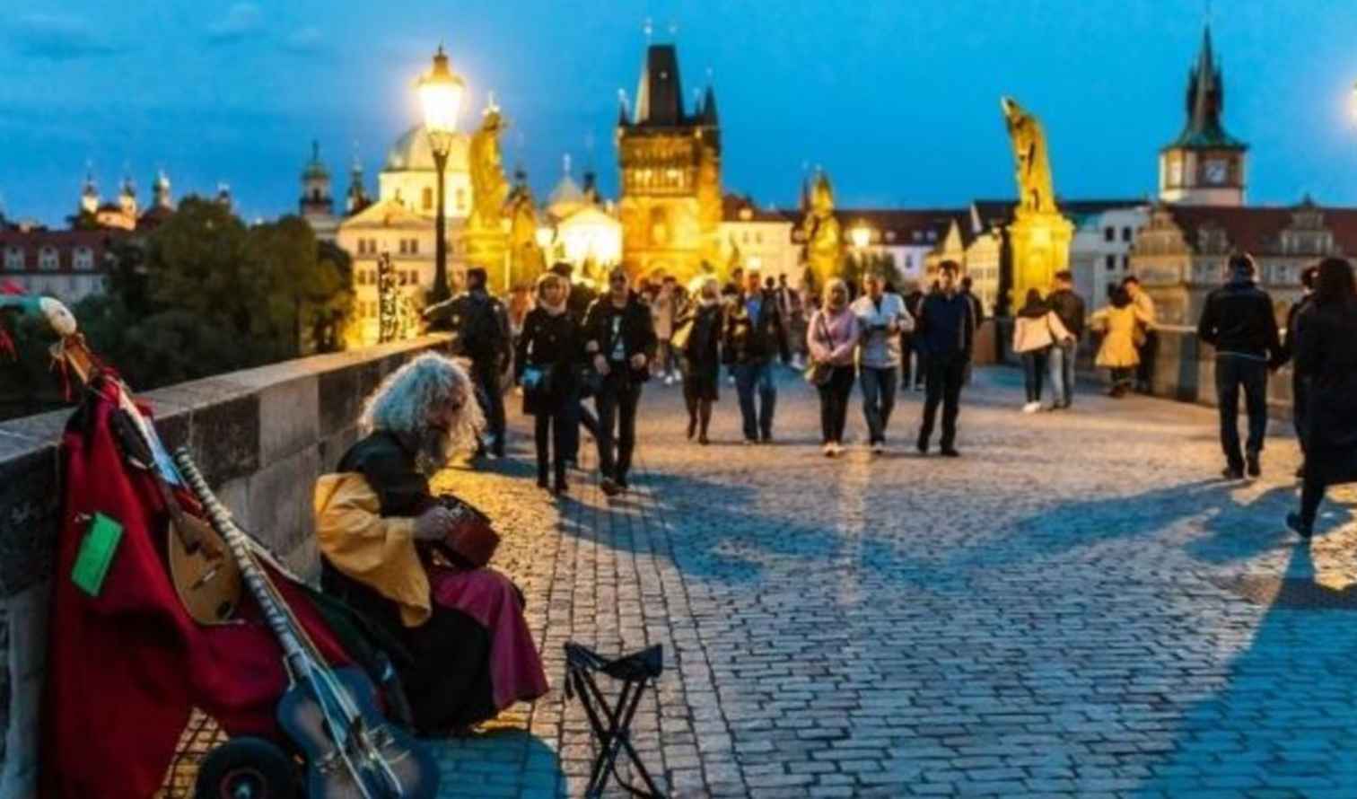 Street musician playing on Charles Bridge in Prague at dusk.