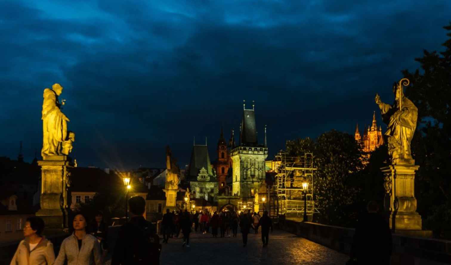 Illuminated statues and tower view on Charles Bridge in Prague during evening.