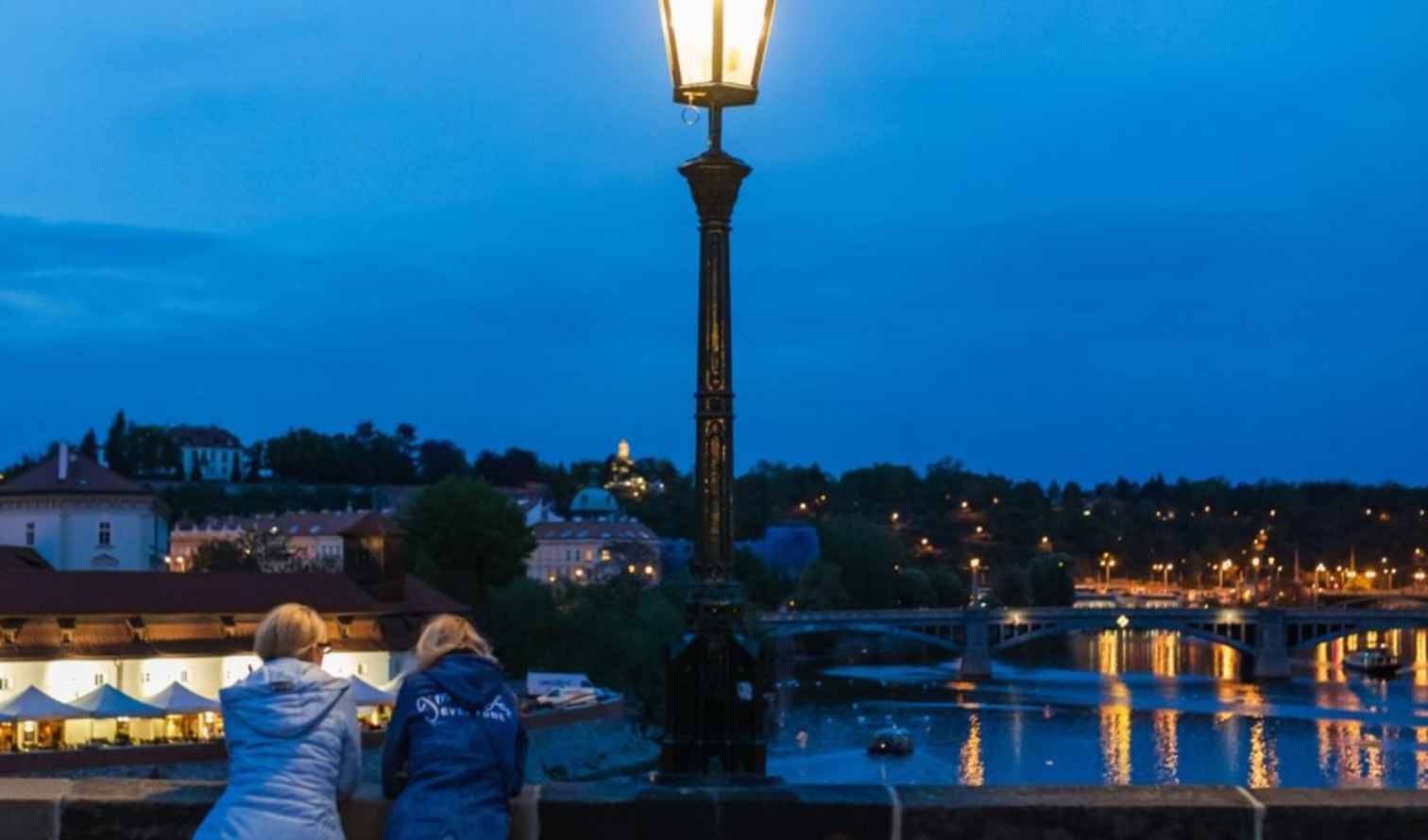 Two people view the Vltava River from Charles Bridge in Prague.