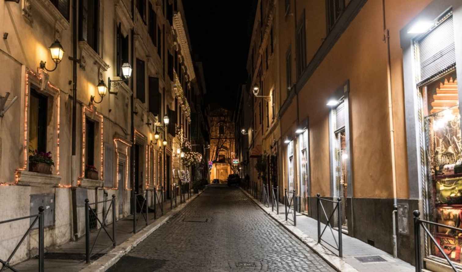 Night scene of a cobblestone alley in Rome featuring decorative building lights.
