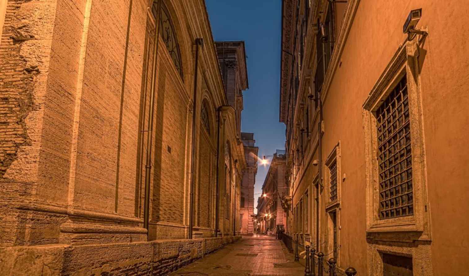 Narrow street in Rome with historical buildings at dusk.