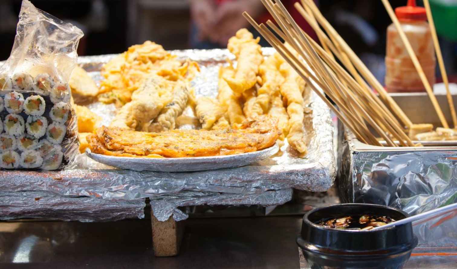 Food stall featuring fried snacks and sushi rolls with dipping sauce in Seoul