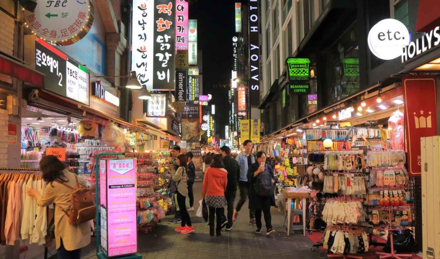 Busy shopping street in Myeongdong, Seoul with various stores and signs.