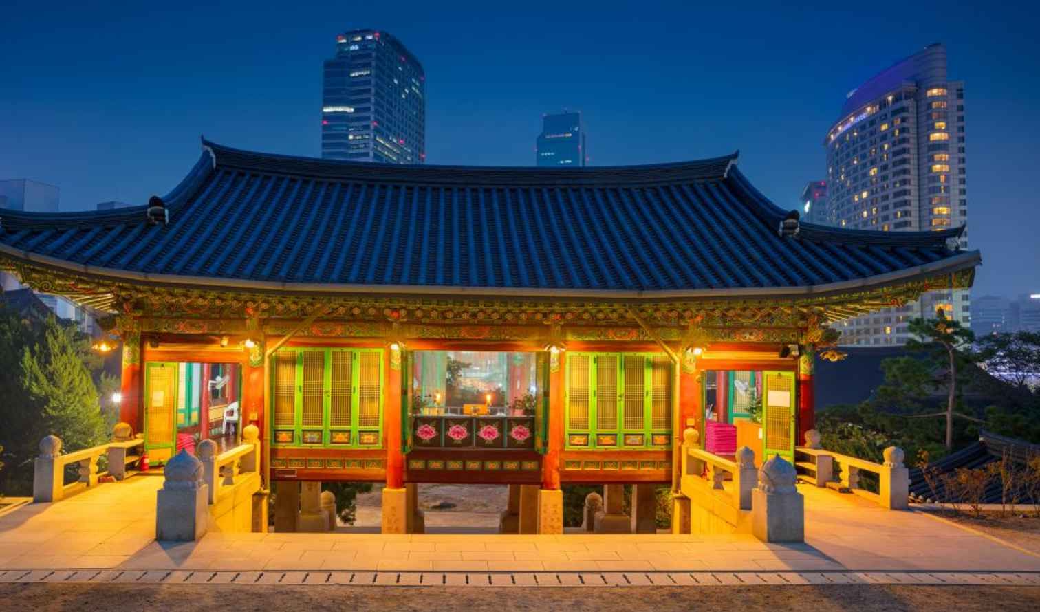 Traditional Korean building with city skyscrapers in Seoul at dusk.