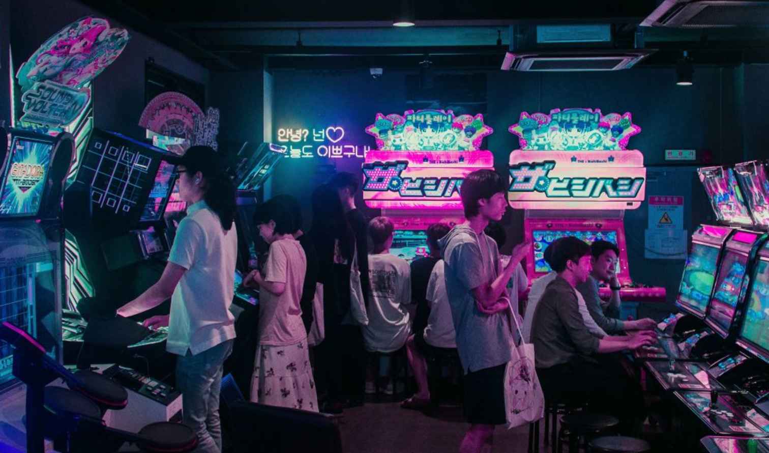 People playing arcade games in a gaming center with neon lights in Seoul