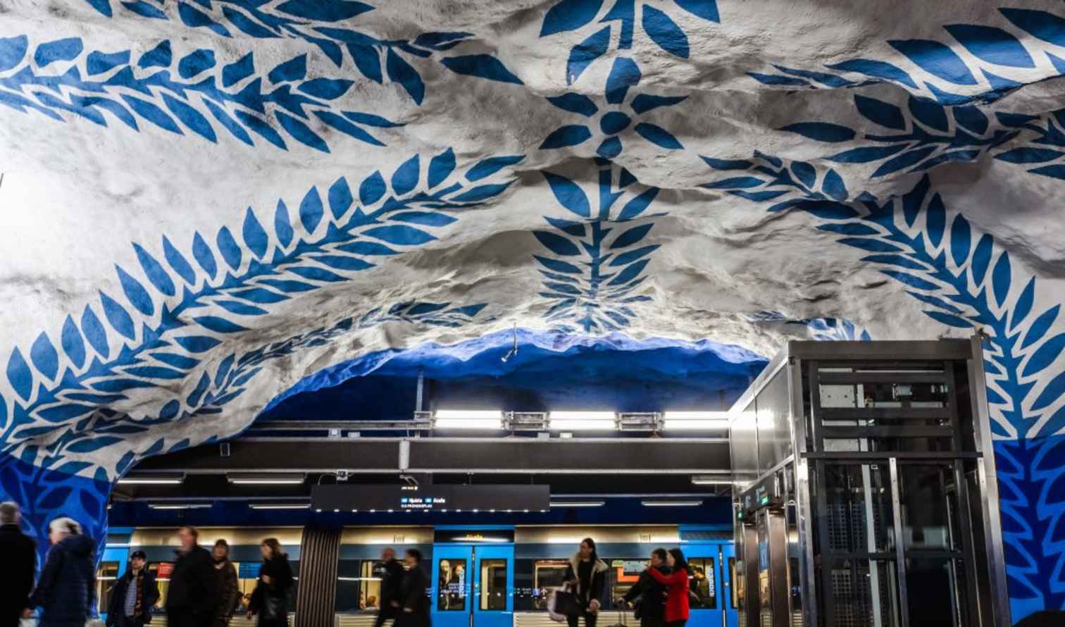 Blue patterned ceiling and commuters inside Stockholm's T-Centralen metro station.