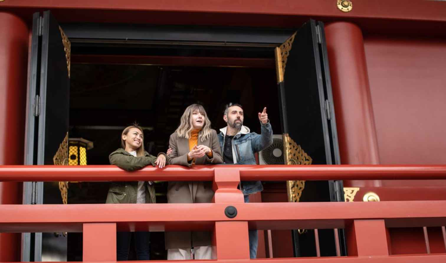 Three people stand on a red balcony at Sensoji Temple in Tokyo, Japan.