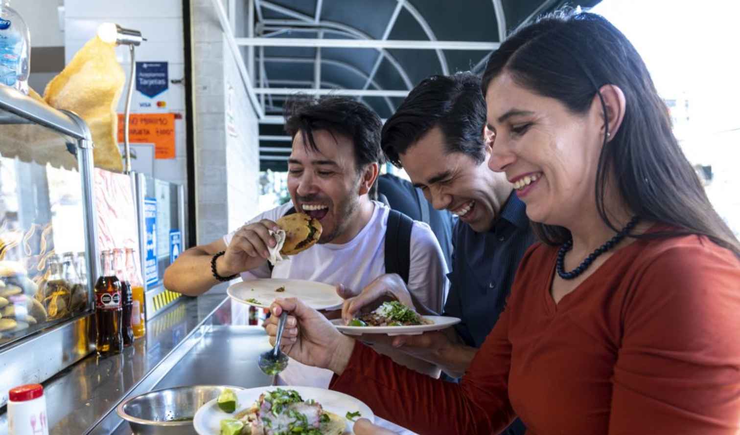 Three people eating tacos at a street food stall in Mexico.