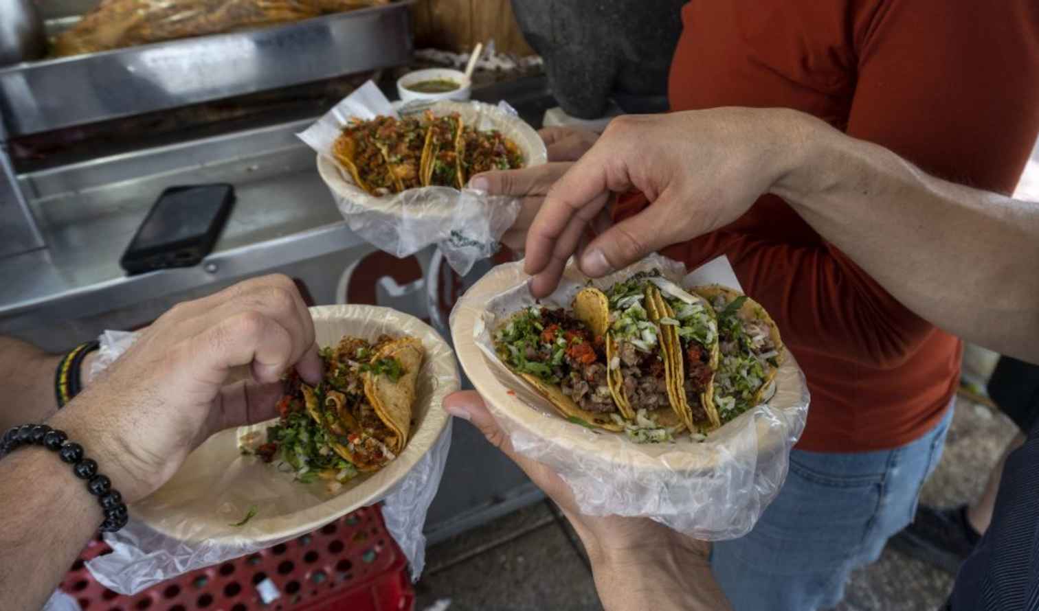 People holding plates of tacos near a street food stall in Mexico City