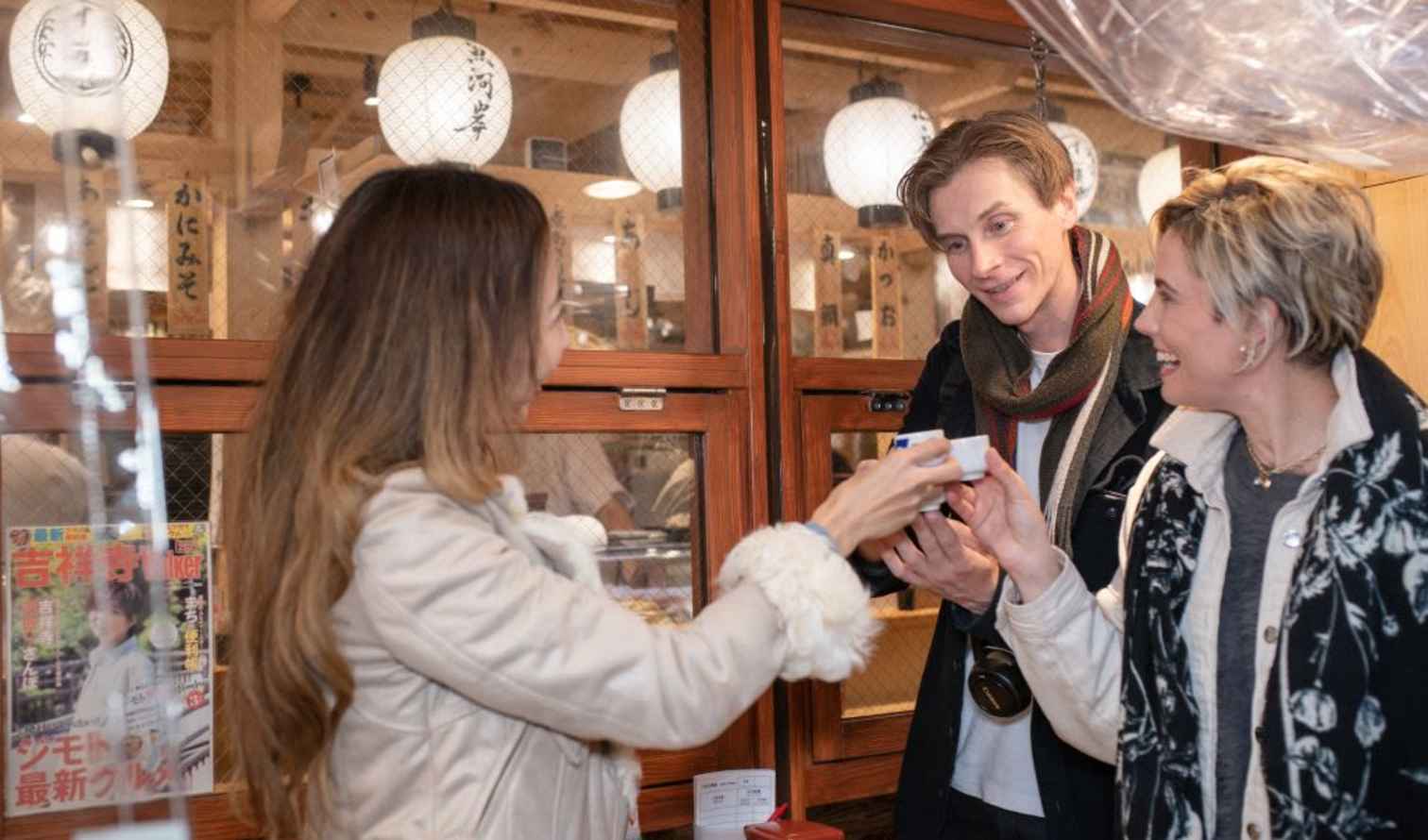 Three people exchanging a small item inside a Japanese restaurant in Tokyo