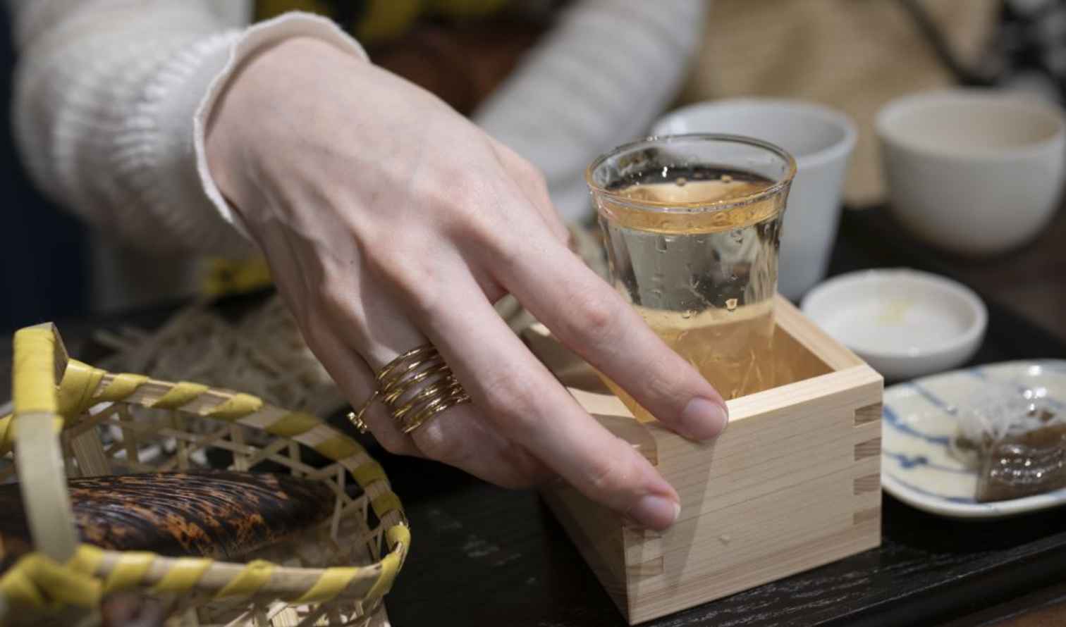 A hand reaches for a glass of sake in a wooden cup in Tokyo