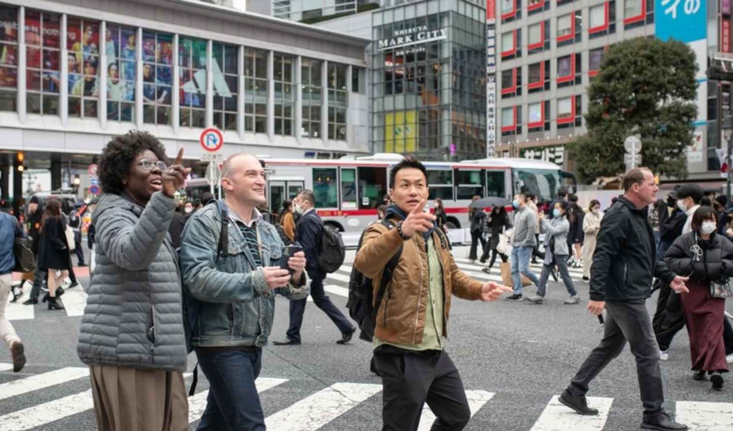 Three individuals walking across the Shibuya Crossing in Tokyo, Japan.