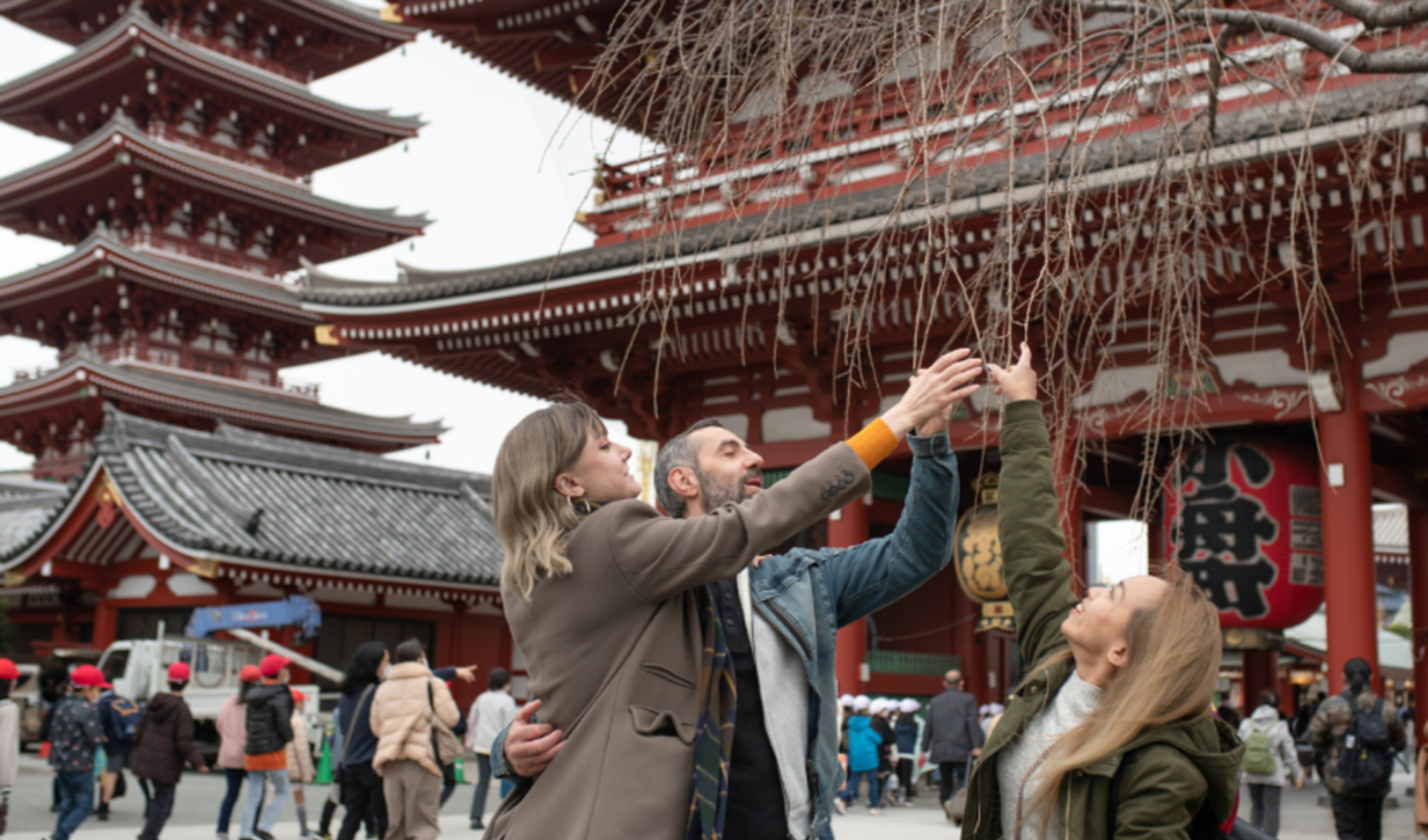 Three people reach for branches near Senso-ji Temple in Tokyo, Japan.