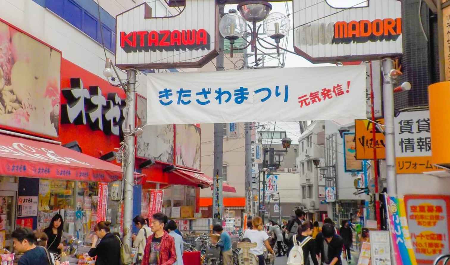 People walking under the Kitazawa shopping street sign in Tokyo.