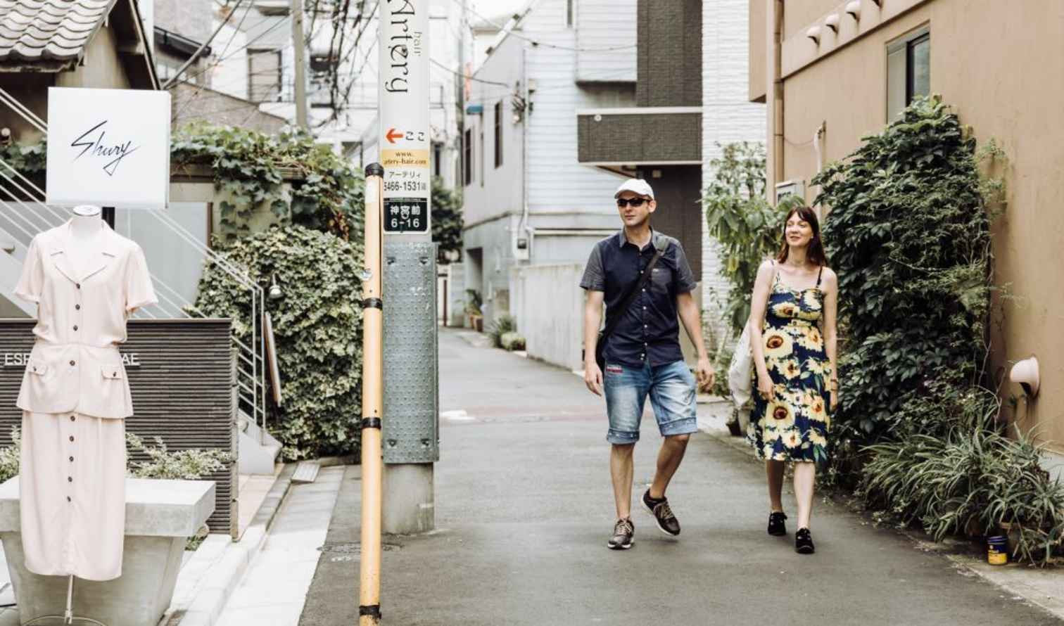 Two people walking down a narrow street in Tokyo with a clothing shop sign.