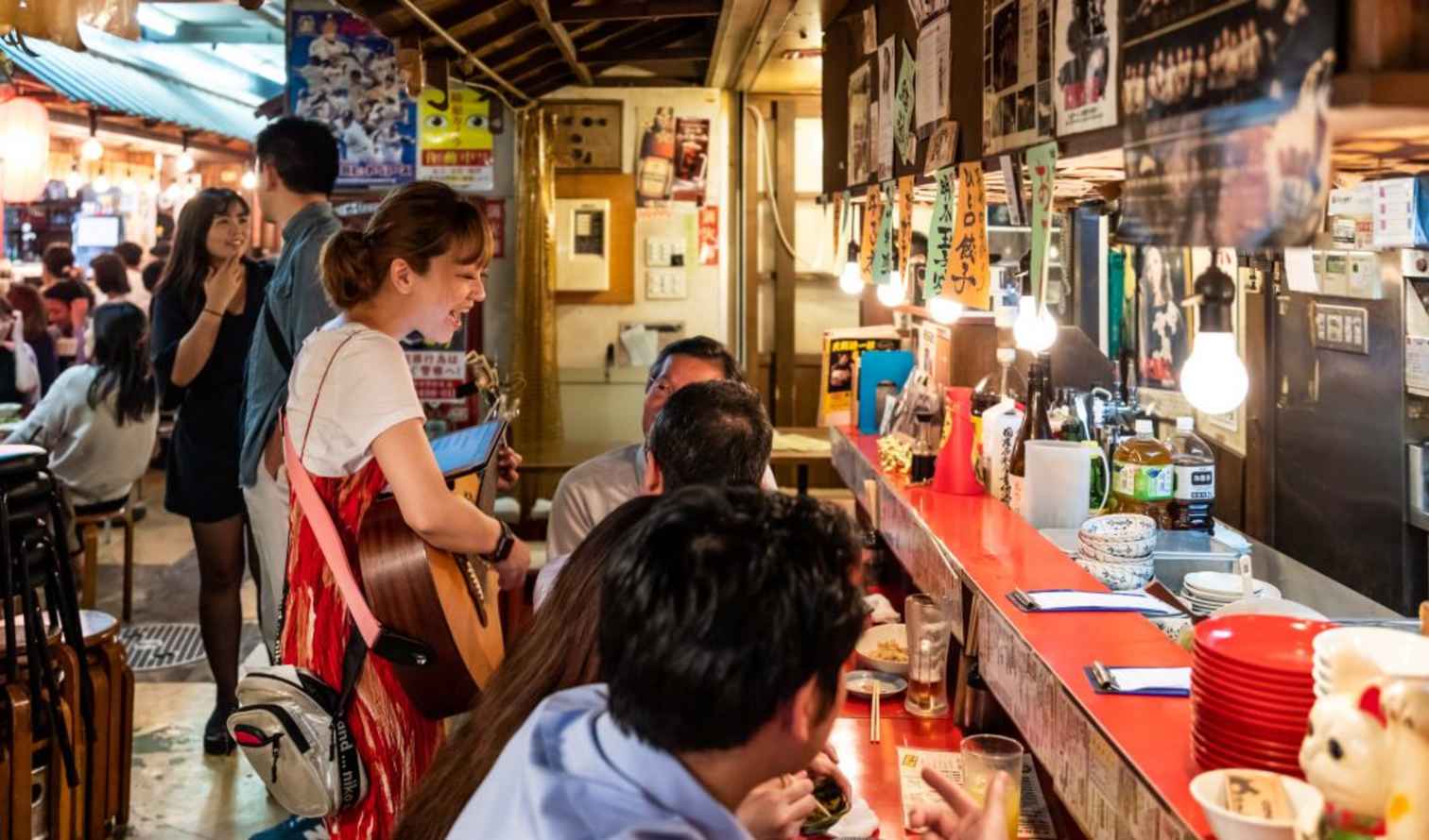 People dining at an izakaya in Tokyo, Japan, with bright hanging lights.