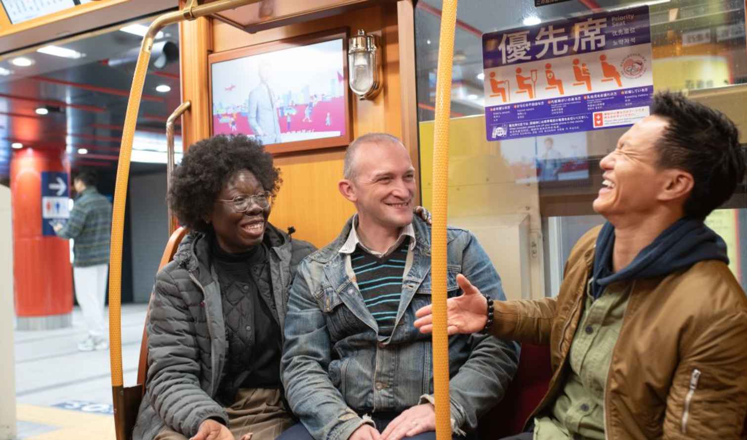 Three people talking inside a tram car with a priority seating sign in Tokyo