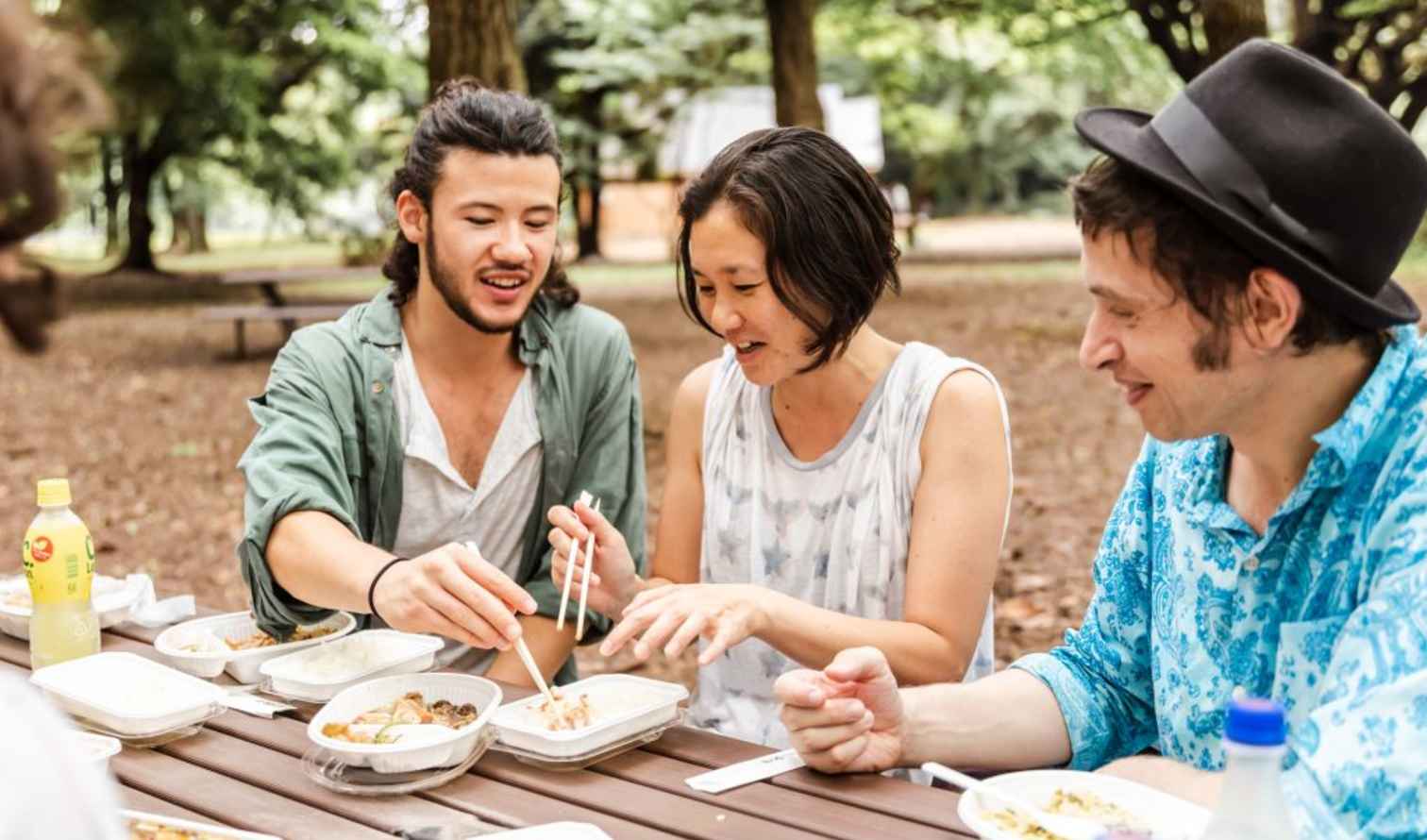 Group of people eating at a wooden picnic table in a park in Tokyo
