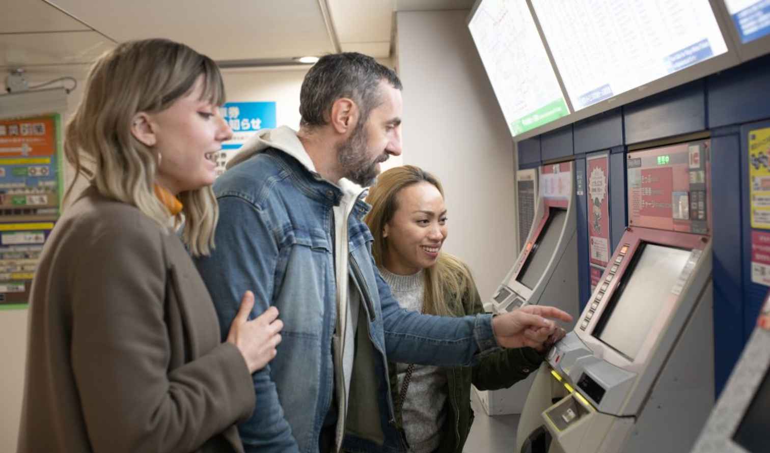 Three people using ticket machines at a Japanese train station in Tokyo