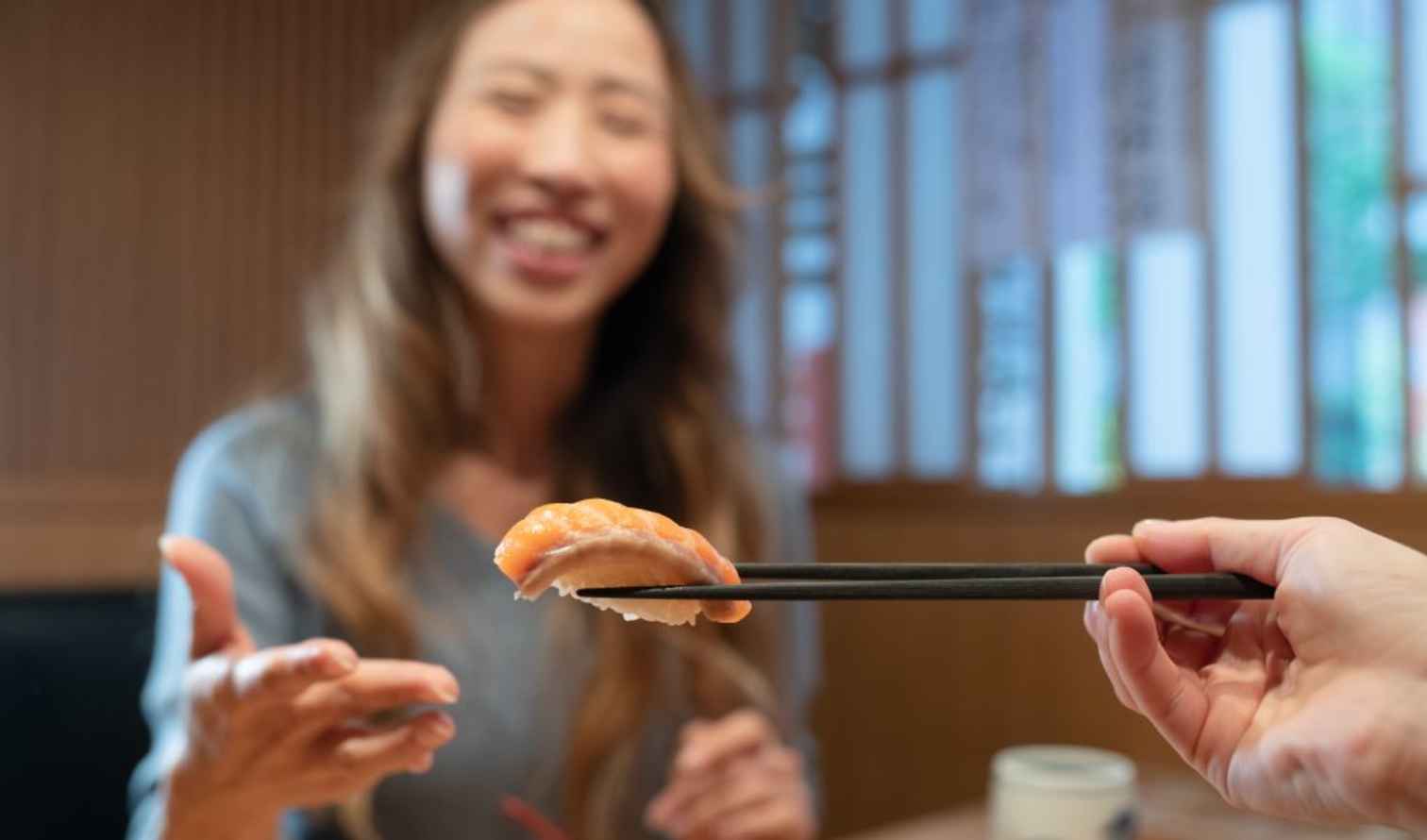Close-up of sushi piece held by chopsticks near a woman in Tokyo