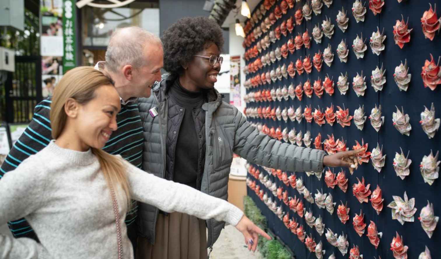 Three people stand in front of a wall of origami flowers at a Japan street display in Tokyo
